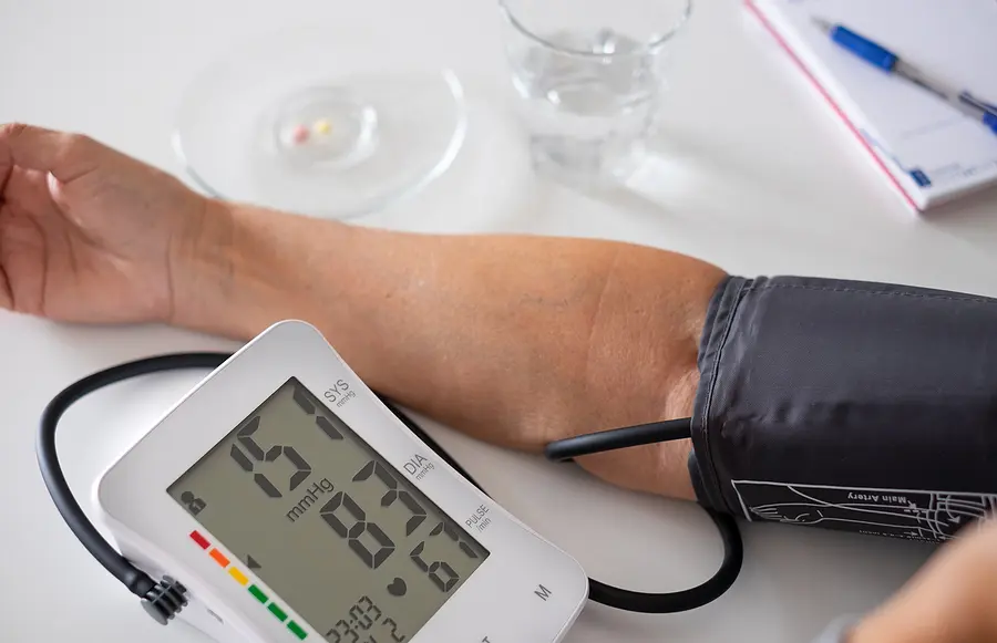 Elderly woman using medical device to measure blood pressure - senior woman suffering from hypertension sitting at home table taking care of her health