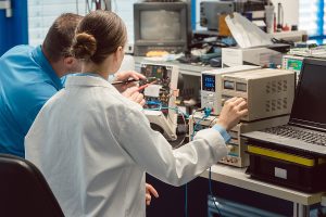 Team of male and female electronic engineers wearing white lab coats and testing a product prototype. 