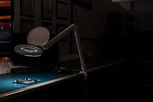 Quality control station in an electronics manufacturing factory with a magnifying lamp with the light on shining down on to a printed populated circuit board ready for a quality check before being finished. 