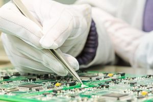 Close up of a gloved hand working on a PCB board. 