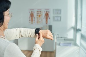 Over the shoulder view of an older woman checking her pulse on fitness tracker at the doctor's office. 