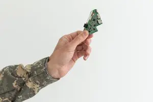 Person in military holding up an electronic chip against a white background. 